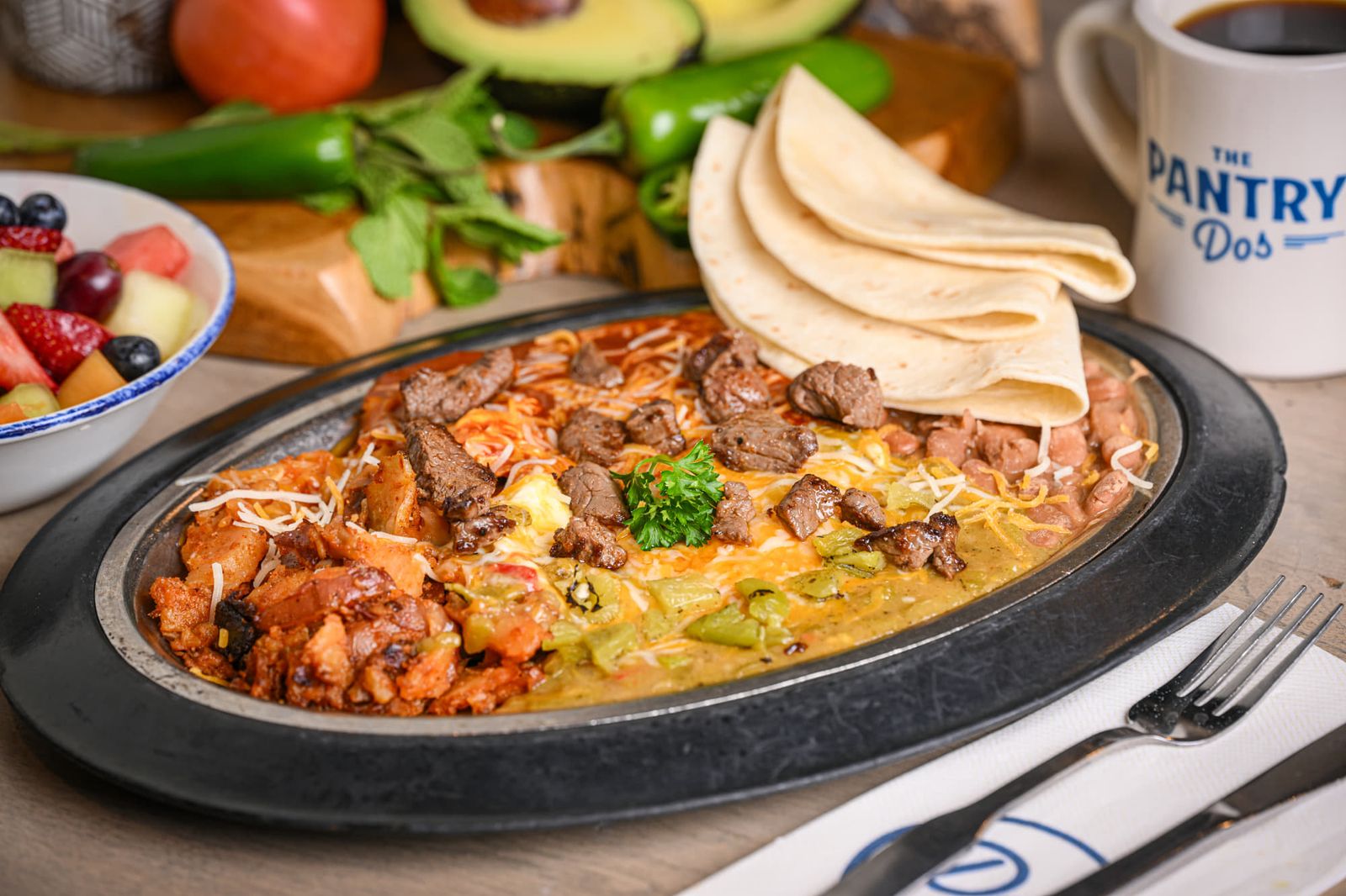 Steak and eggs smothered in red and green chile and cheese on a hot skillet with potatoes, beans and flour tortillas